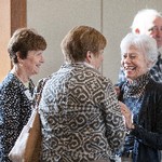 Three smiling women are standing in a small group, while a man standing behind them looks at the camera